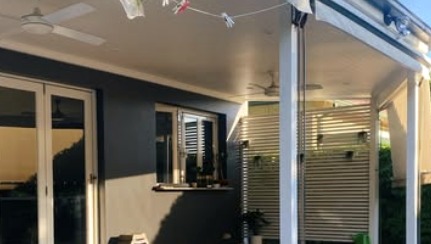 Covered patio with ceiling fan beside a dark clad home